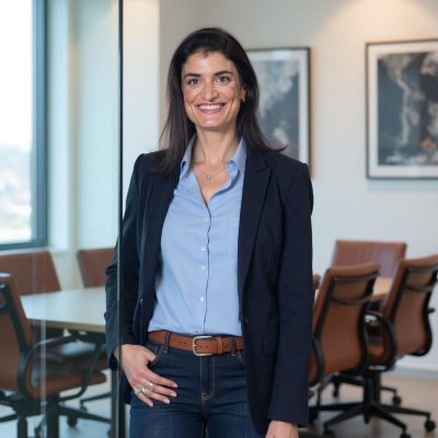 עורכת הדין בחולצה תכולה ובז׳קט כהה בחדר ישיבות